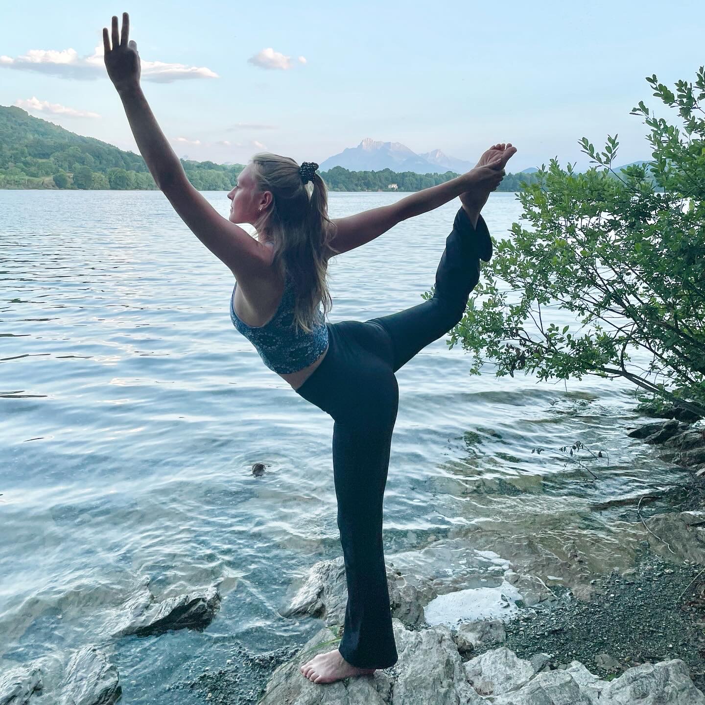 Manon en posture du danseur au bord d'un lac, face aux montagnes près de Grenoble